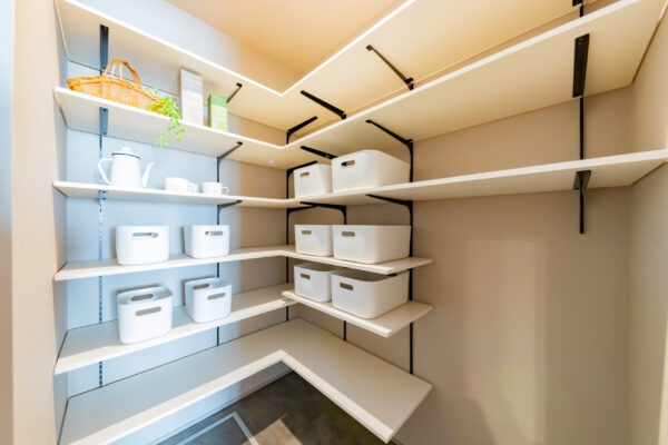 空間を最大限に活用した、L字型の可動棚が設置された大容量のシューズクローク。高さ調節が可能な白い棚板と黒のスチールブラケットが、シンプルで清潔感のある玄関収納を実現しています。